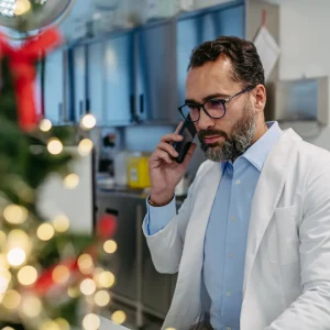 Business man answering phone with a Christmas tree in the background.